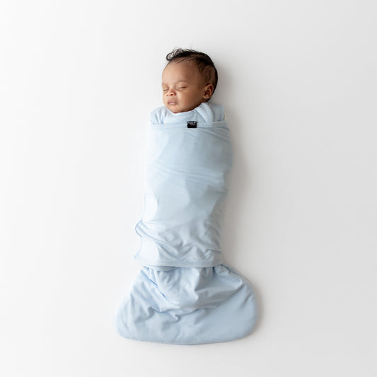 Baby swaddled in a kyte baby sleep bag swaddler in a light blue color