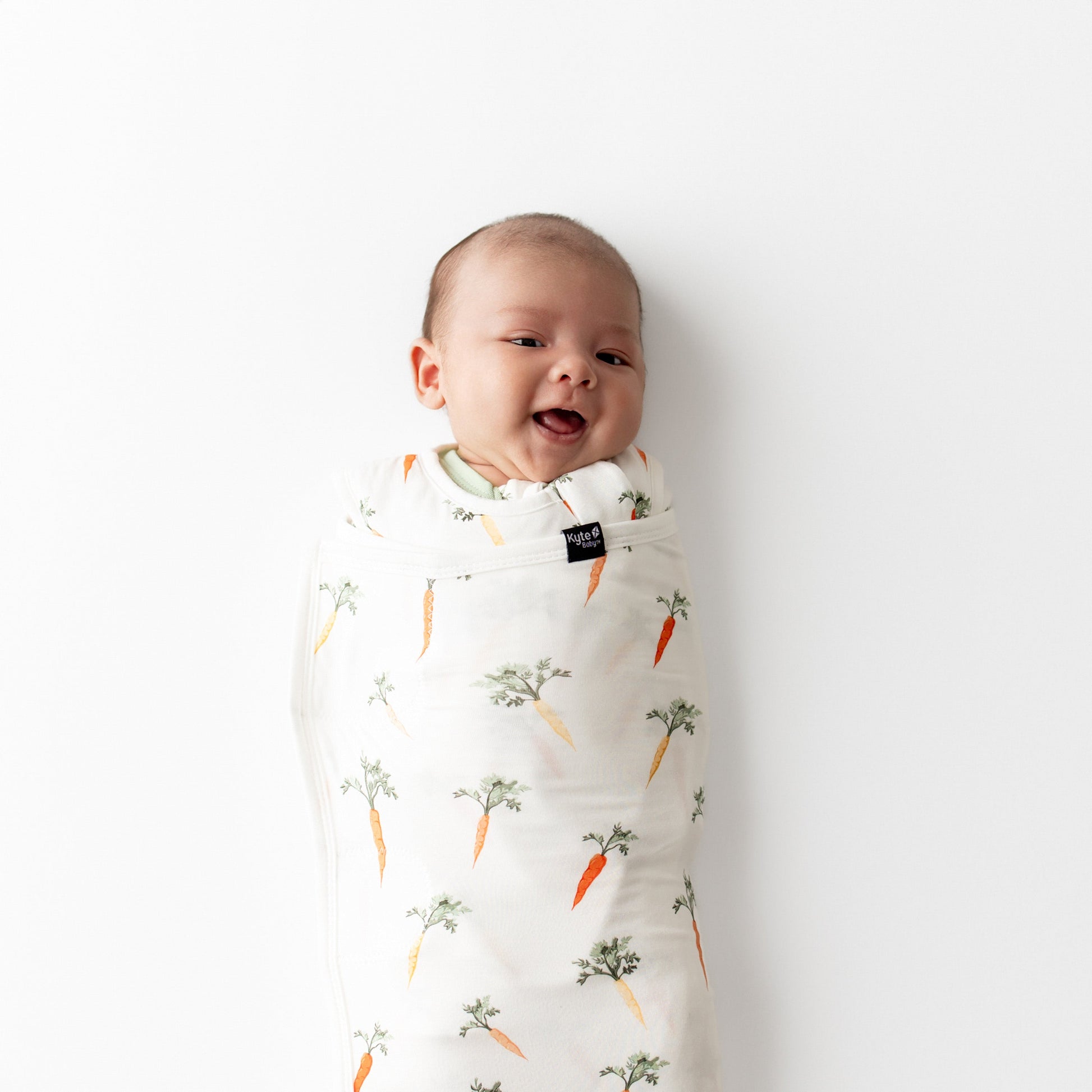 Close up of newborn swaddled in the Sleep Bag Swaddler in Carrot 1.0 laying on a white surface