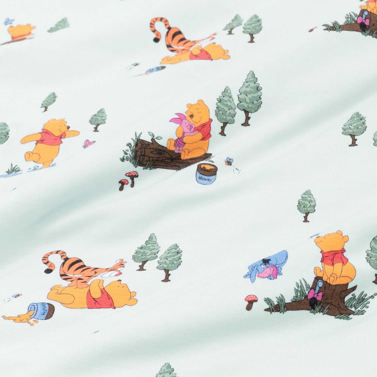 Close up of fabric swatch of the Winnie the Pooh Hundred Acre Wood showing the book characters on a light green background