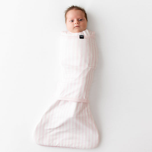 Newborn laying on a white surface swaddled in the Sleep Bag Swaddler in Small Sakura Stripe 1.0
