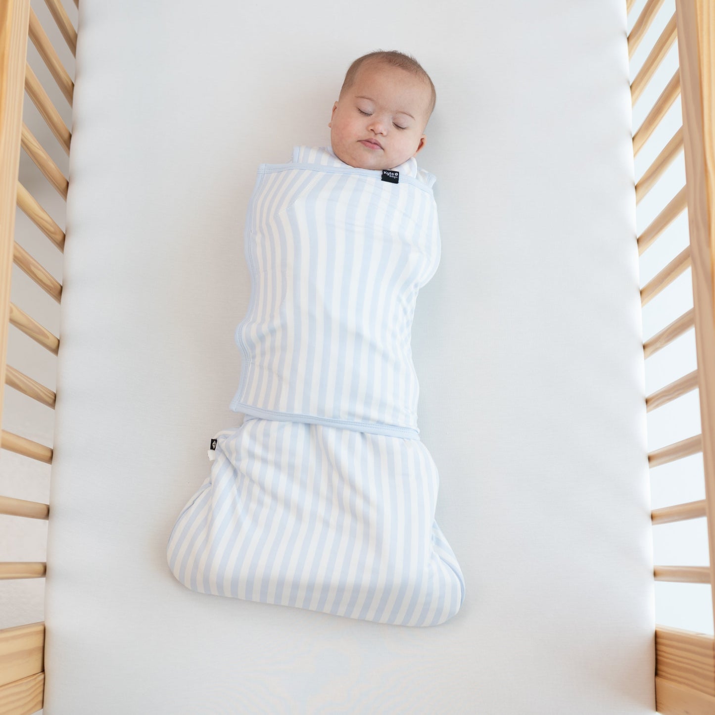 Sleeping Baby laying in a crib swaddled in the Sleep Bag Swaddler in Small Mist Stripe 1.0