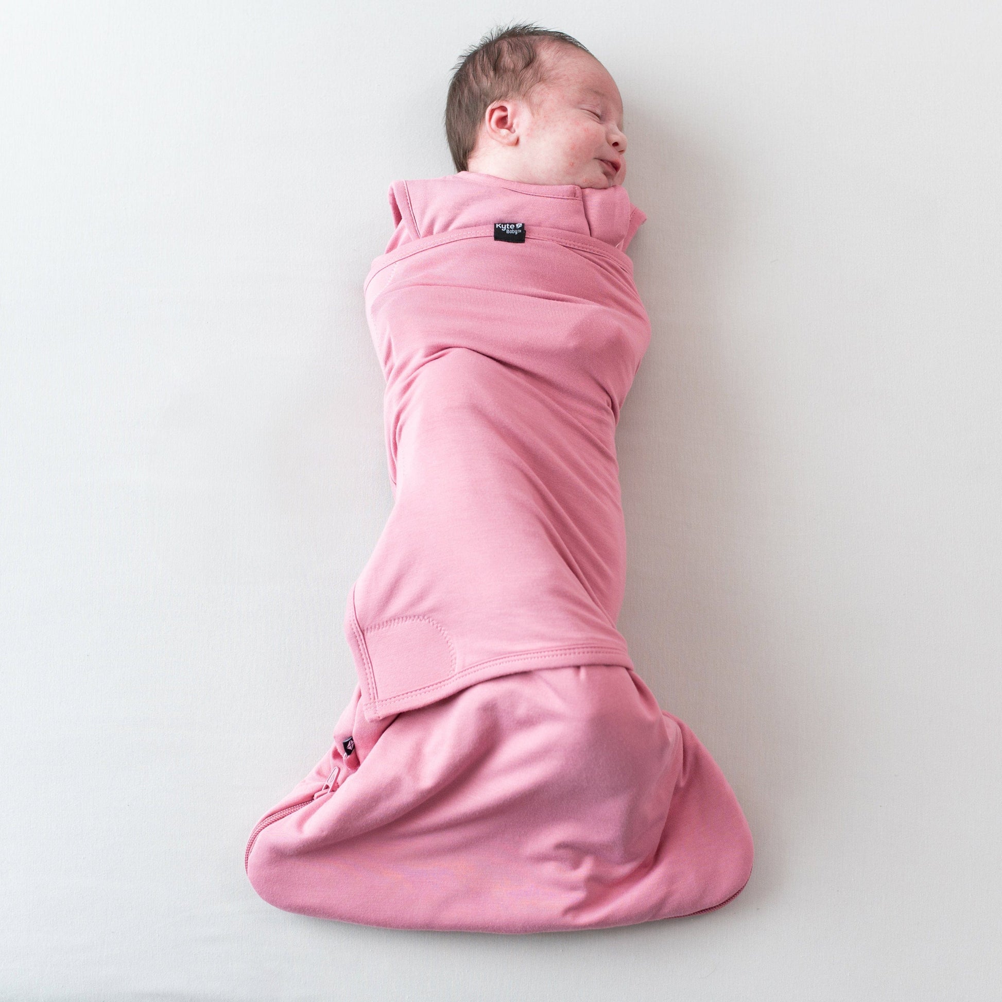 Newborn swaddled in Kyte Baby Sleep Bag Swaddler in Apple Blossom with elastic band