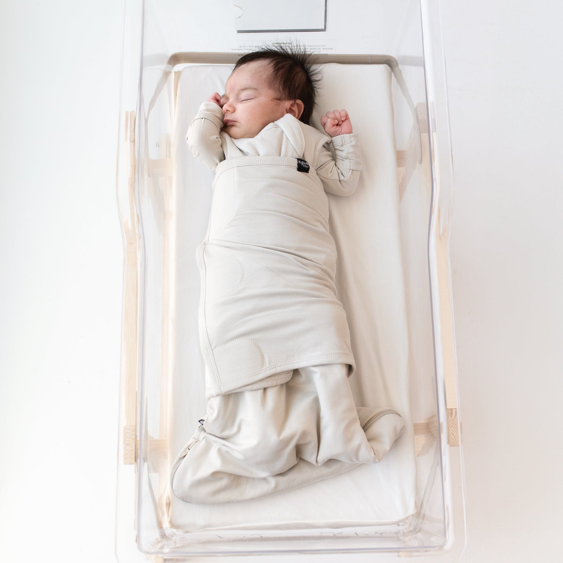 Baby sleeping in bassinet while swaddled in the Sleep Bag Swaddler in Oat 1.0 